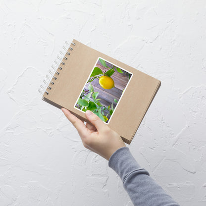 Lifestyle photo of a rectangular vinyl sticker with an image of a bright yellow lemon budding branches, placed on a small notepad.