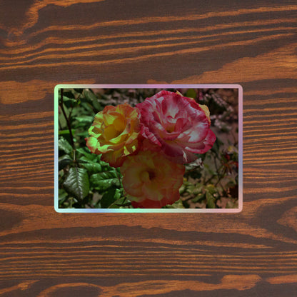 Lifestyle photo of a rectangular holographic sticker with a close-up image of three pink and yellow multicolored roses, placed on a brown wooden table surface.
