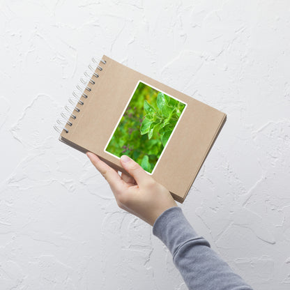 Lifestyle photo of a rectangular vinyl sticker with an image of an oregano sprig in an herb garden, placed on a small notepad.