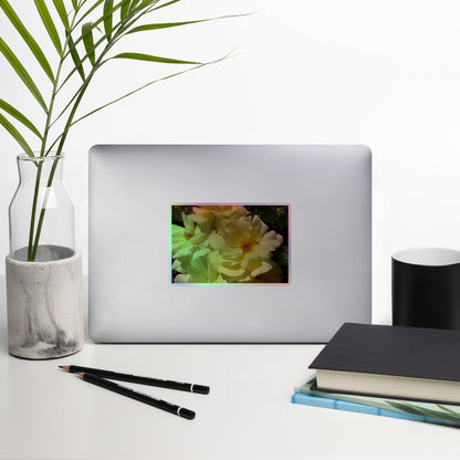 Lifestyle photo of a rectangular holographic sticker with an image of off-white rose blooms with visible stamen, placed on a laptop with desk supplies nearby.