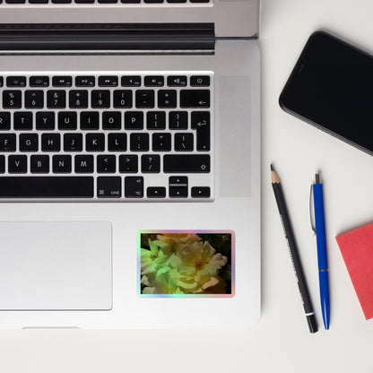 Lifestyle photo of a rectangular holographic sticker with an image of off-white rose blooms with visible stamen, placed on a laptop to the right of the mouse pad.