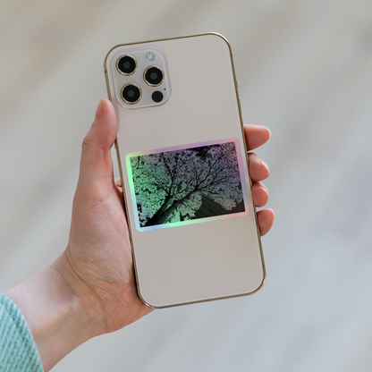Lifestyle photo of a rectangular holographic sticker with an image of a dark embossed tree lightning design, placed on the back of a phone.