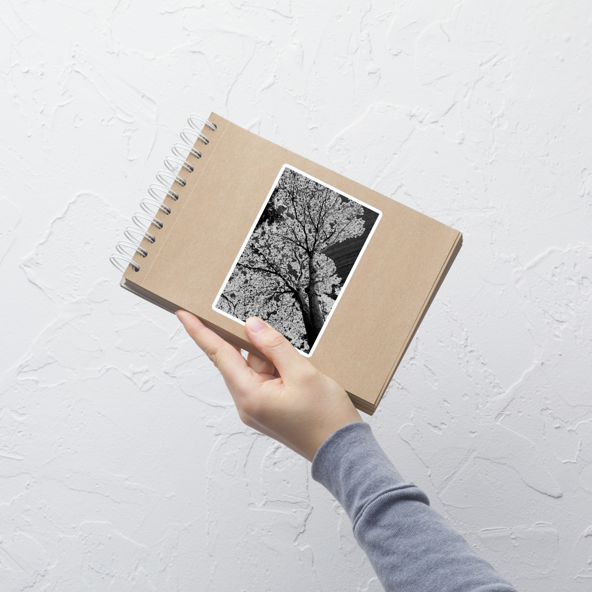 Lifestyle photo of a rectangular vinyl sticker with an image of an dark embossed tree design with lightning like features, placed on a small notepad.