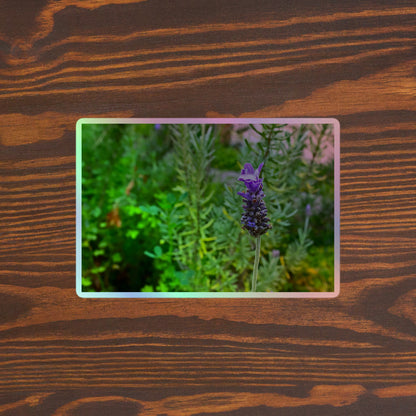 Lifestyle photo of a rectangular holographic sticker with an image of a purple lavender bloom in an herb garden, placed on a brown wooden table surface.