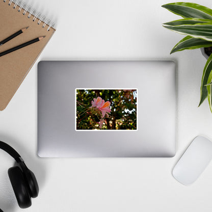 Lifestyle photo of a rectangular vinyl sticker with an image of light pink azaleas with orange accents, placed on the outside of a laptop.