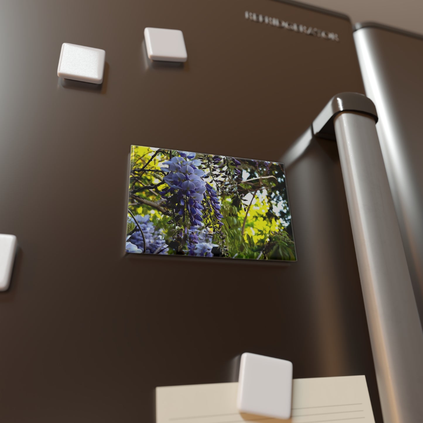 Lifestyle photo of a rectangular button magnet with an image of vibrant green leaves and purple wisteria flowers in the foreground, placed on a fridge.