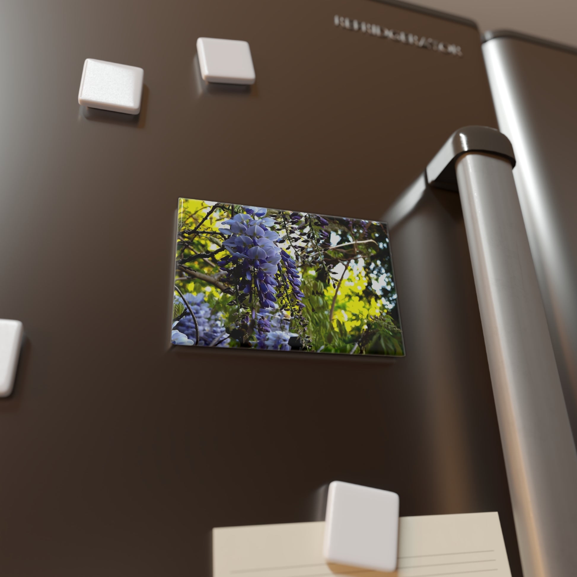 Lifestyle photo of a rectangular button magnet with an image of vibrant green leaves and purple wisteria flowers in the foreground, placed on a fridge.
