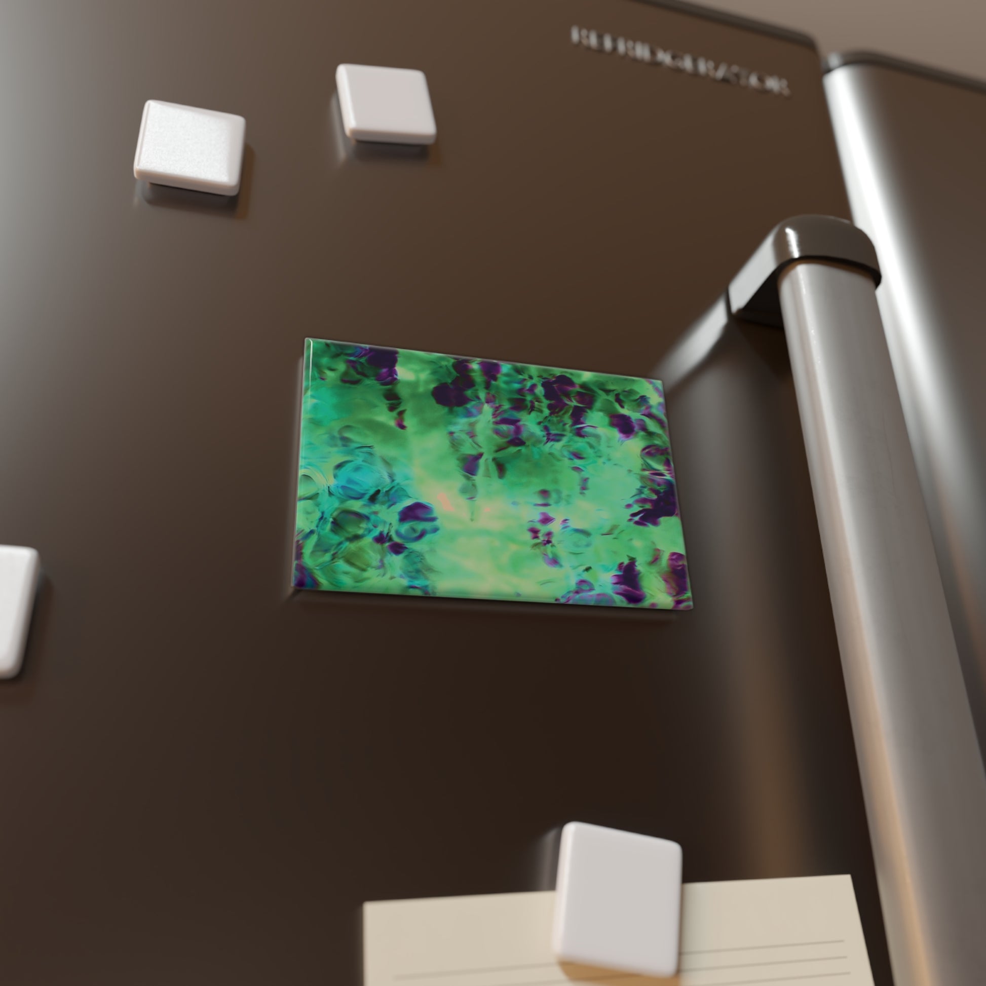 Lifestyle photo of a rectangular button magnet with an image of a vivid green and purple water reflection design, placed on a fridge.