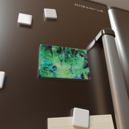 Lifestyle photo of a rectangular button magnet with an image of a vivid green and purple water reflection design, placed on a fridge.