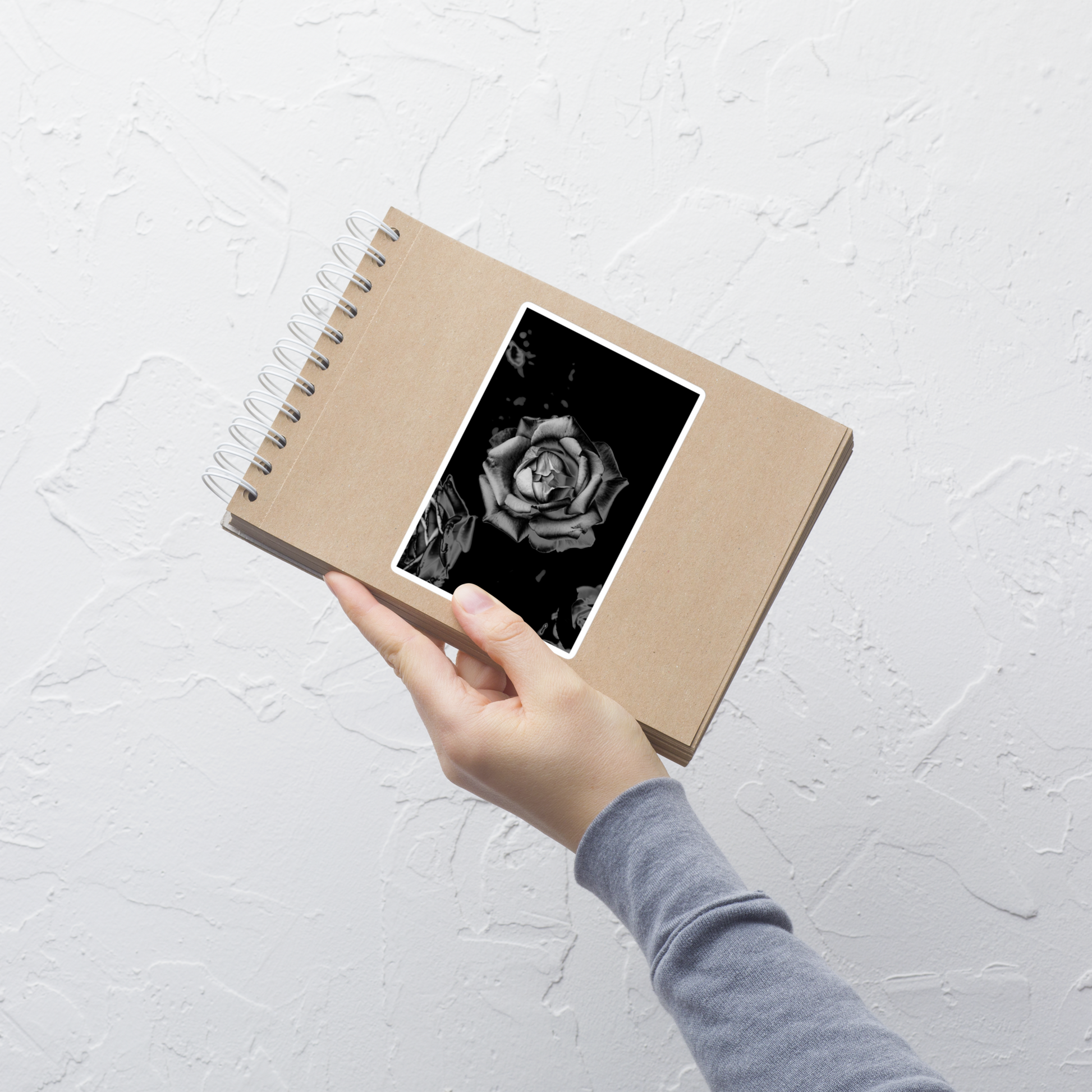 Lifestyle photo of a rectangular vinyl sticker with an image of a grey charcoal rose design, placed on a small notepad.