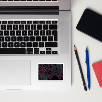 Lifestyle photo of a rectangular vinyl sticker with an image of a neon pink and turquoise tree design with lightning like features, placed on a laptop to the right of the mouse pad.