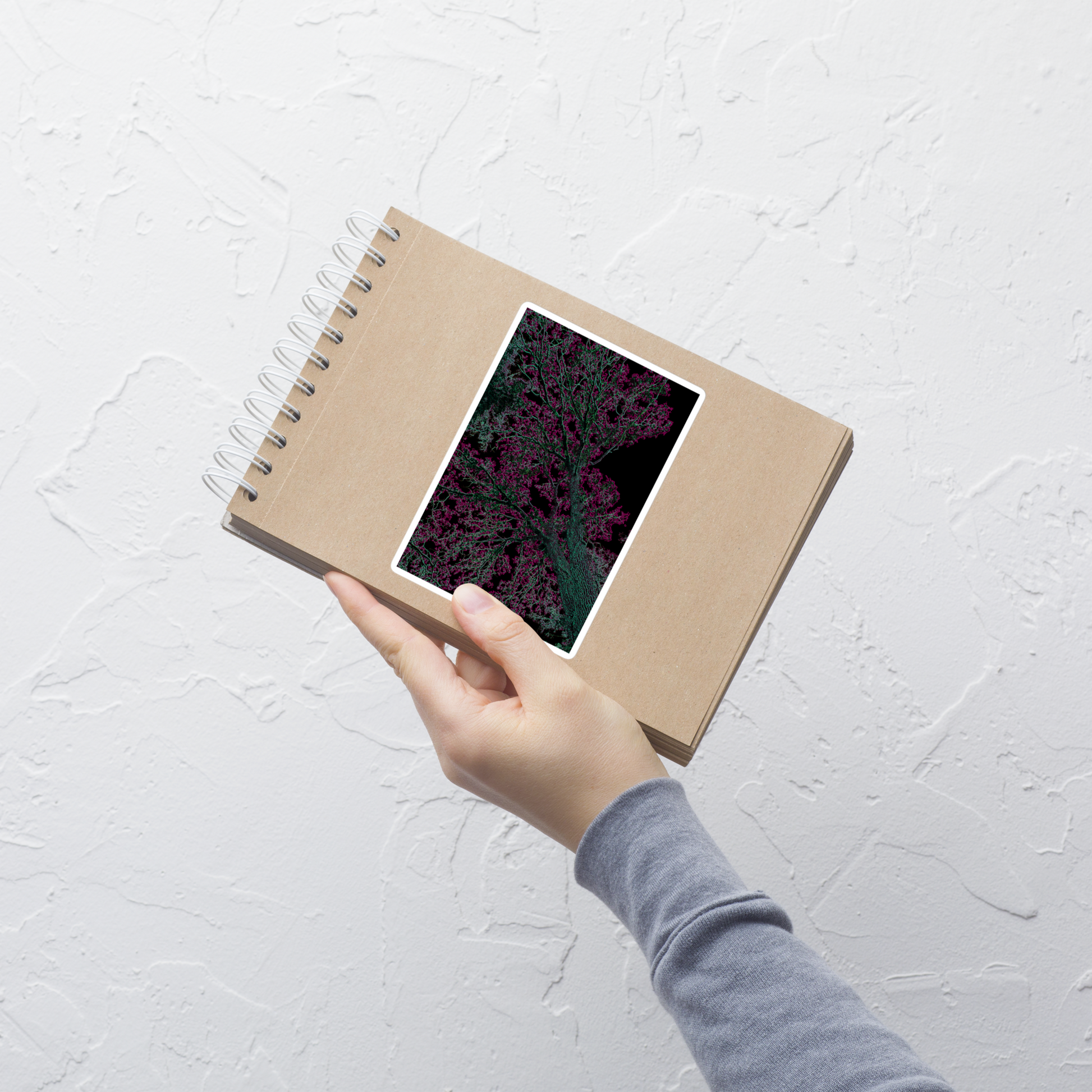Lifestyle photo of a rectangular vinyl sticker with an image of a neon pink and turquoise tree design with lightning like features, placed on a small notepad.