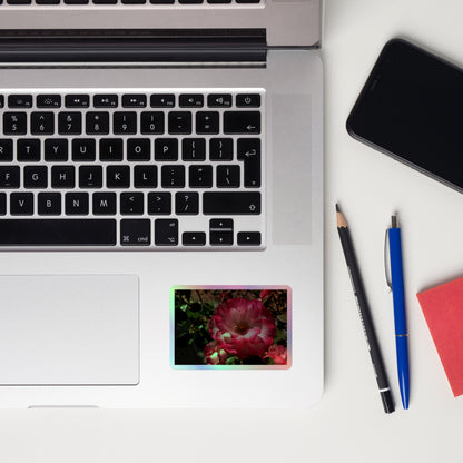 Lifestyle photo of a rectangular holographic sticker with an image of bright pink rose blooms with white centers, placed on a laptop to the right of the mouse pad.