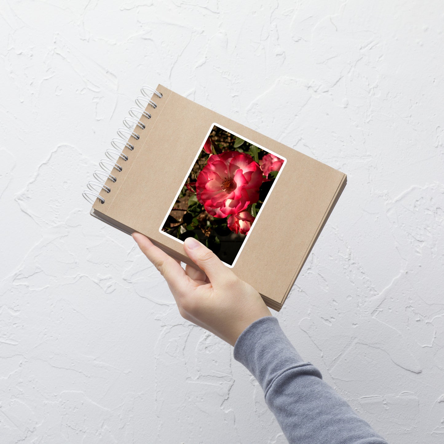 Lifestyle photo of a rectangular vinyl sticker with an image of a pink and white rose, placed on a small notepad.