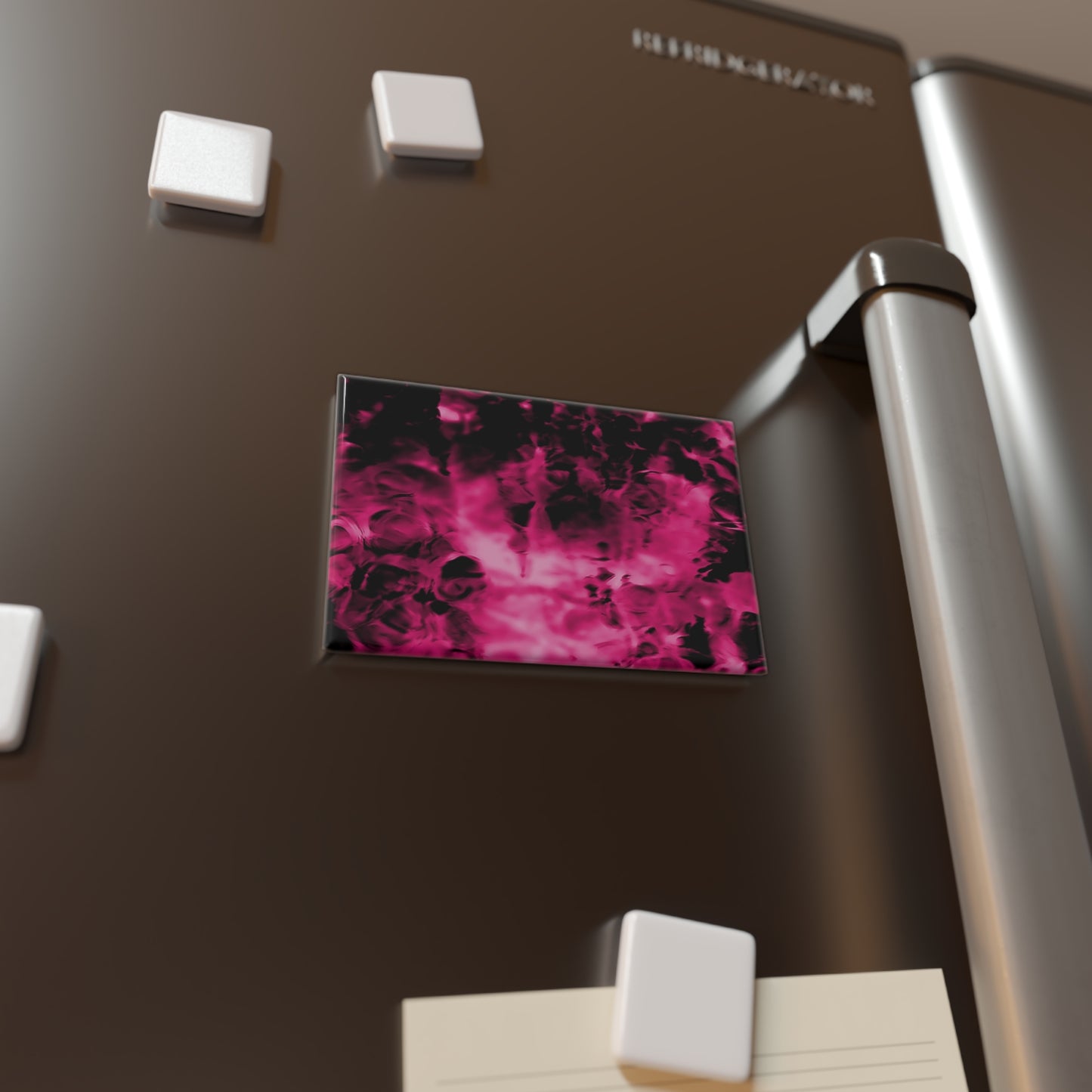 Lifestyle photo of a rectangular button magnet with an image of a vivid pink and black water reflection design, placed on a fridge.