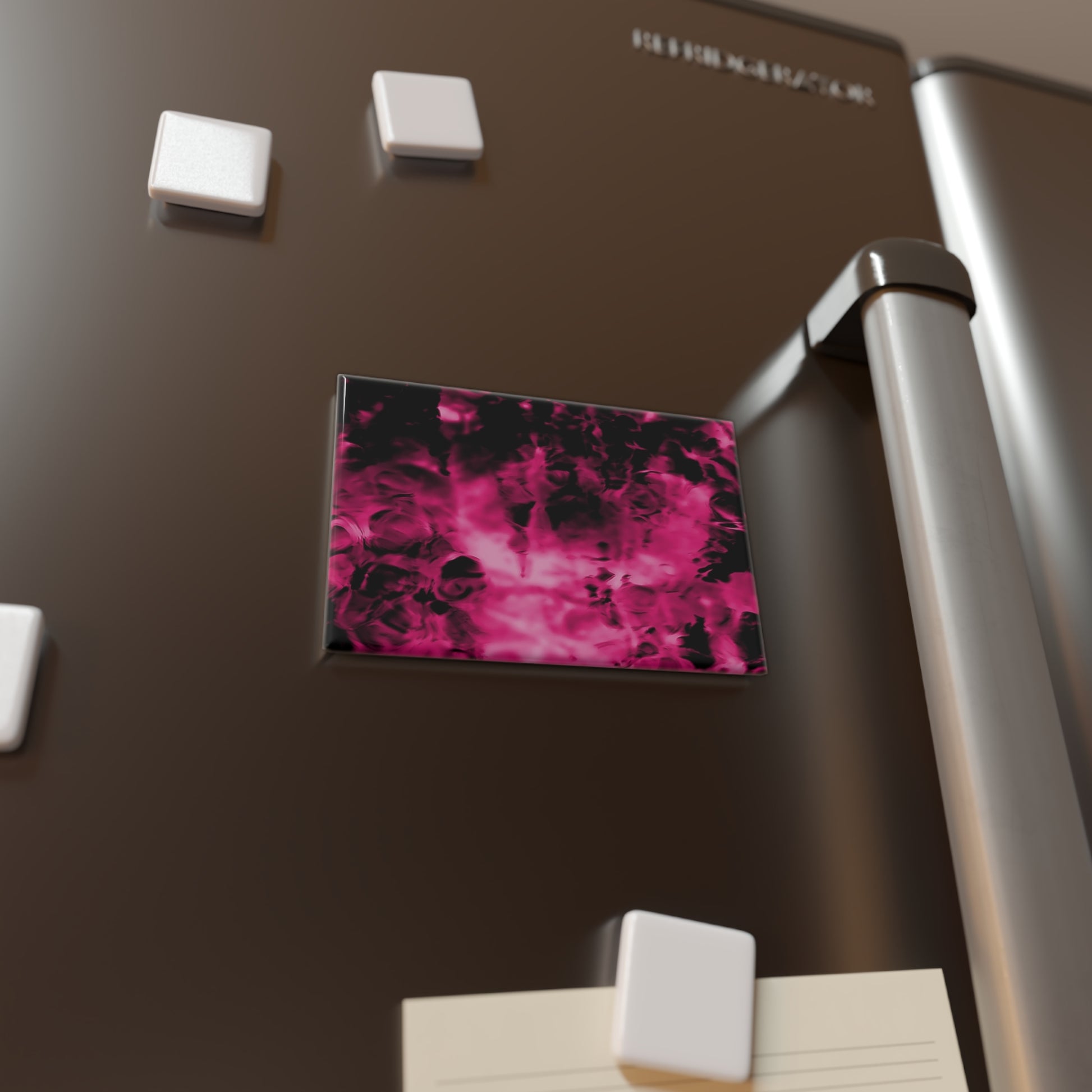 Lifestyle photo of a rectangular button magnet with an image of a vivid pink and black water reflection design, placed on a fridge.