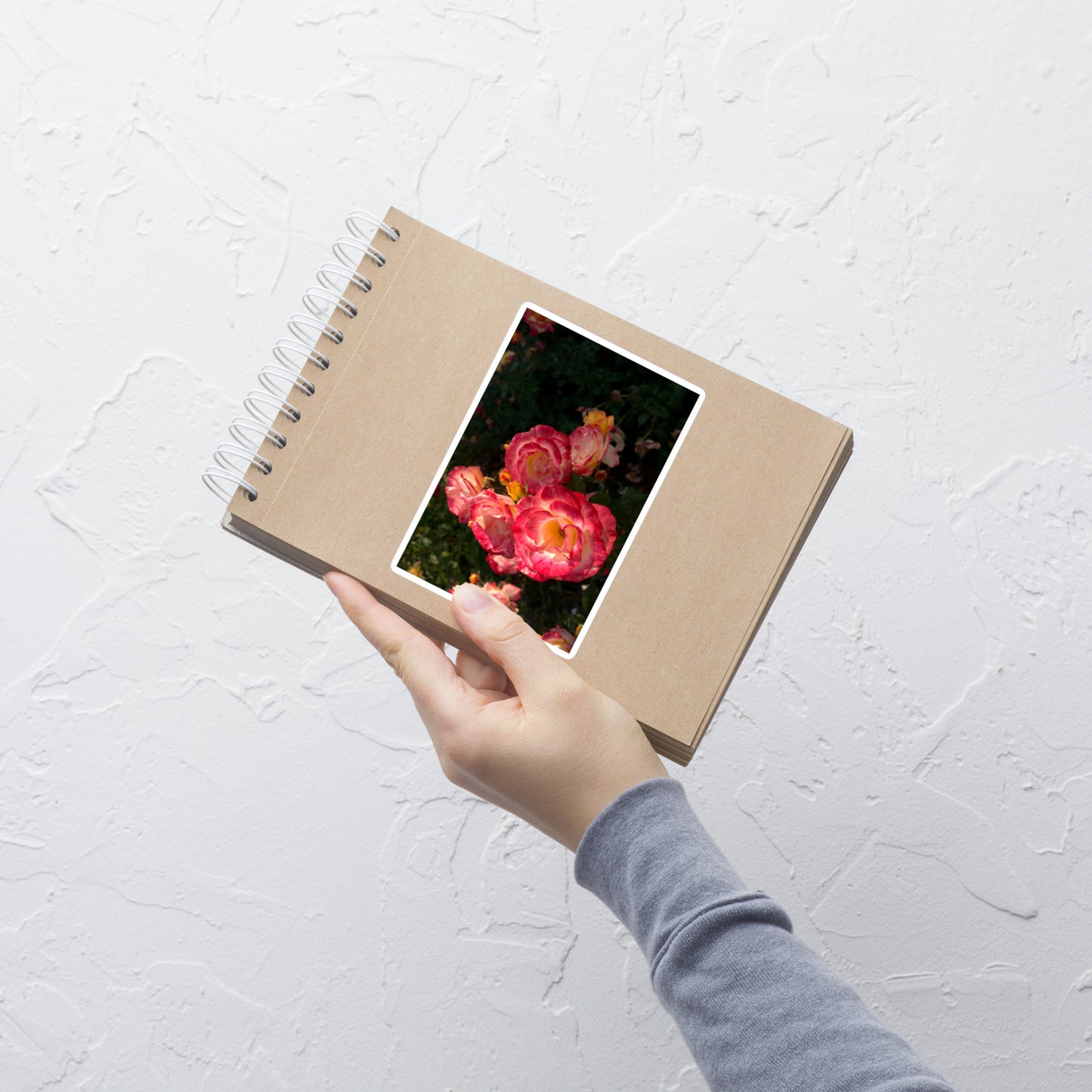 Lifestyle photo of a rectangular vinyl sticker with an image of a garden with pink, yellow, and white roses, placed on a small notepad.