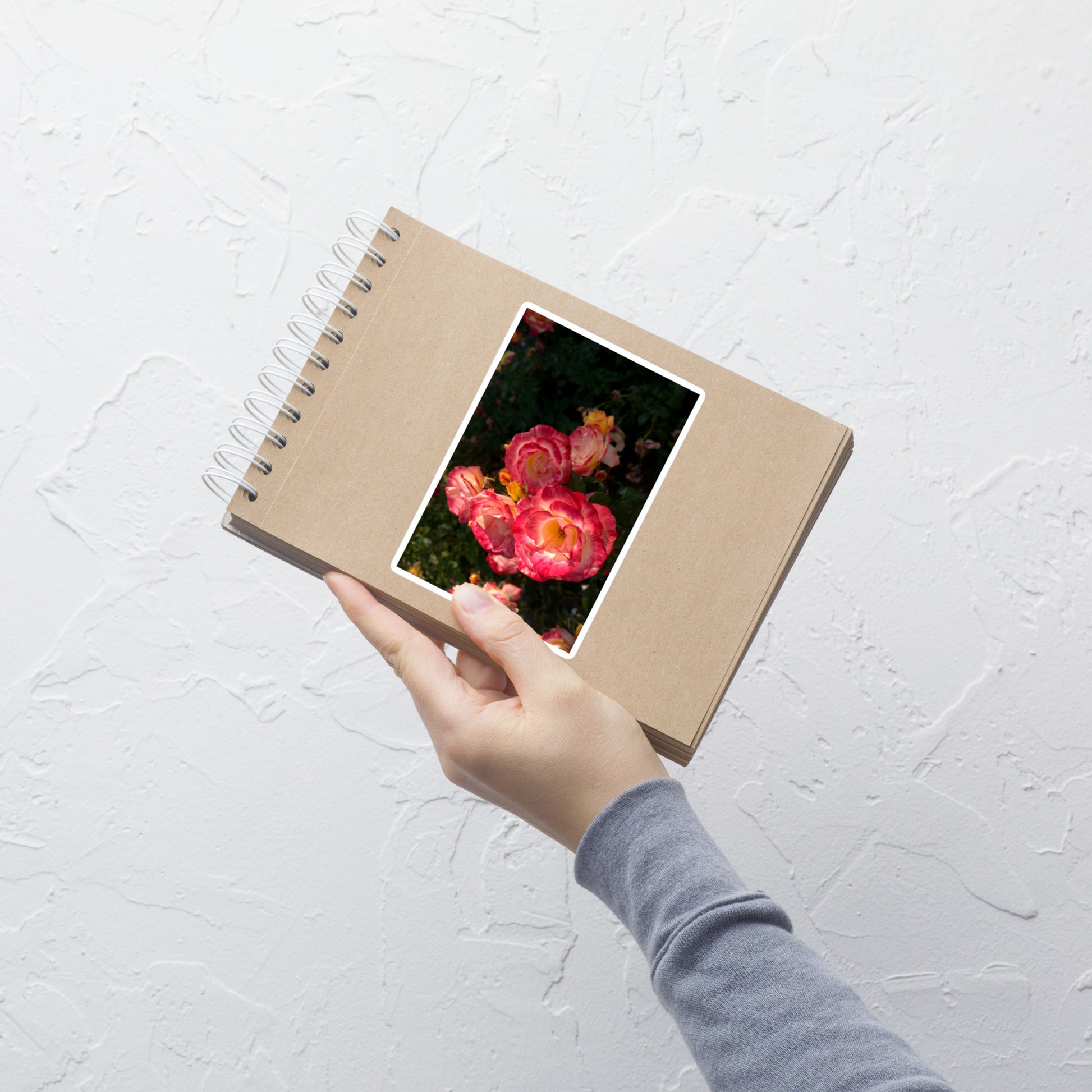 Lifestyle photo of a rectangular vinyl sticker with an image of a garden with pink, yellow, and white roses, placed on a small notepad.