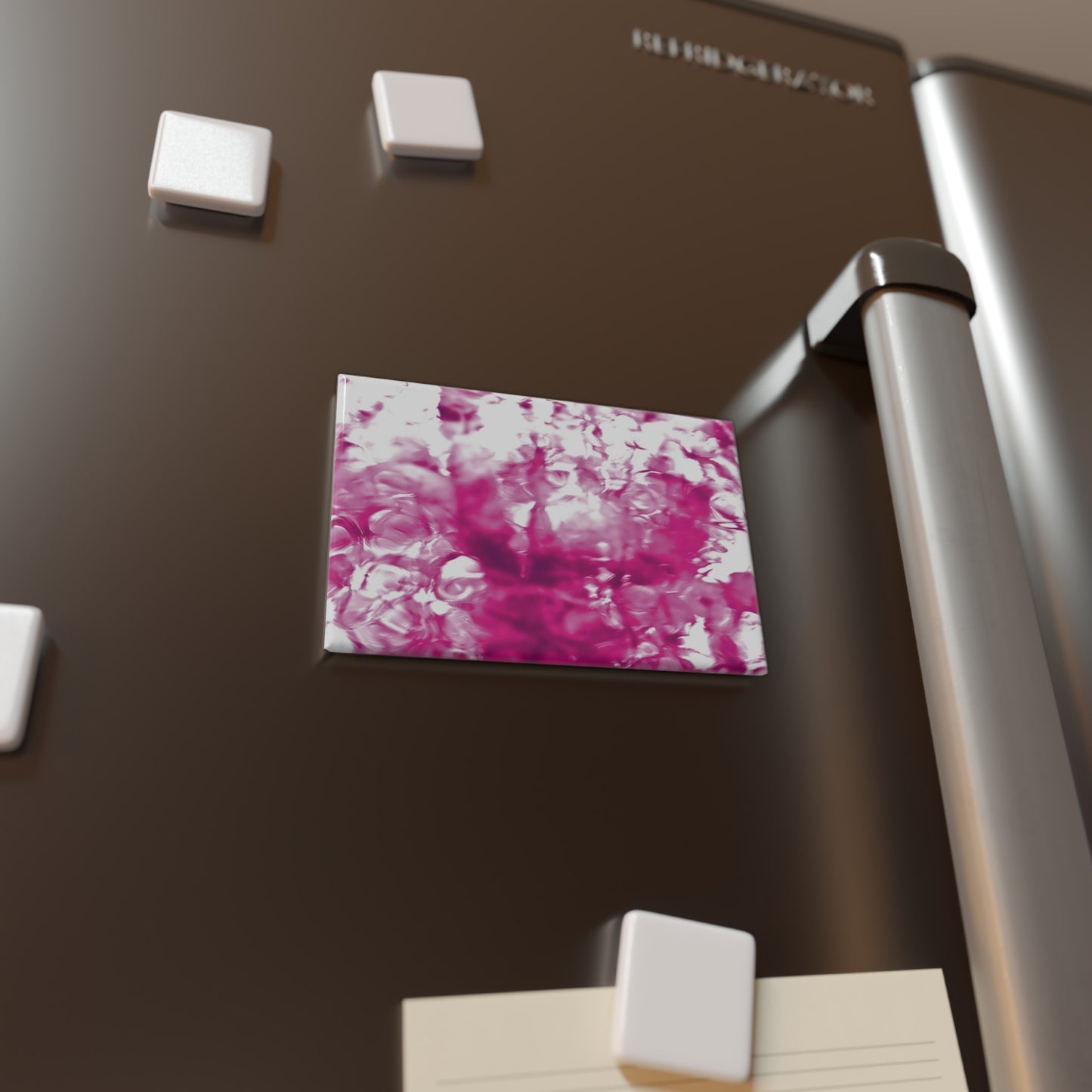 Lifestyle photo of a rectangular button magnet with an image of a vivid pink water reflection design, placed on a fridge.