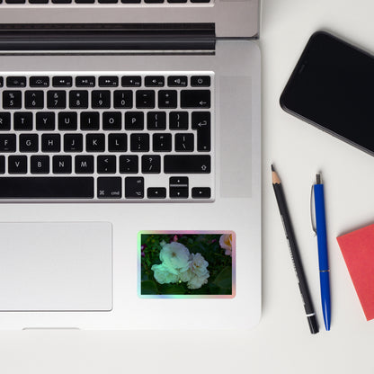 Lifestyle photo of a rectangular holographic sticker with an image of a cluster of white roses with dark green leaves, placed on a laptop to the right of the mouse pad.