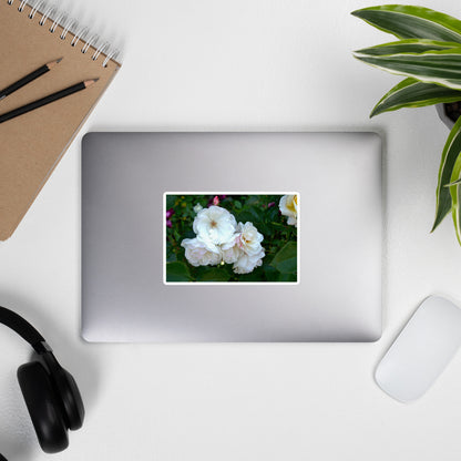 Lifestyle photo of a rectangular vinyl sticker with an image of white roses among dark green leaves, placed on the outside of a laptop.