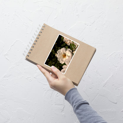 Lifestyle photo of a rectangular vinyl sticker with an image of a white rose with a honeybee on it, placed on a small notepad.