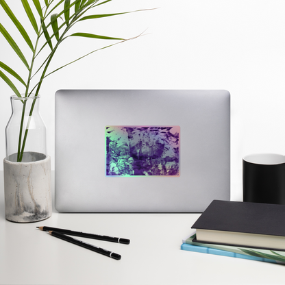 Lifestyle photo of a rectangular holographic sticker with an image of a vivid purple water reflection design, placed on a laptop with desk supplies nearby.
