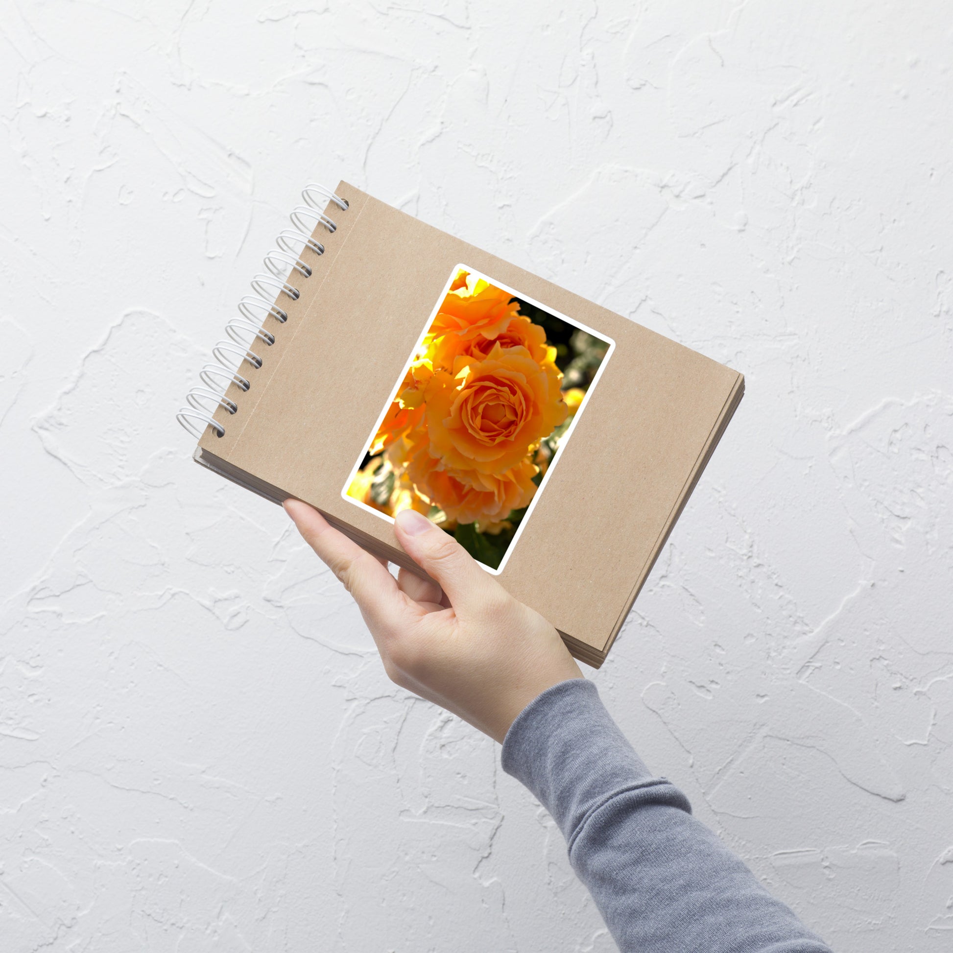 Lifestyle photo of a rectangular vinyl sticker with an image of orange rose blooms, placed on a small notepad.