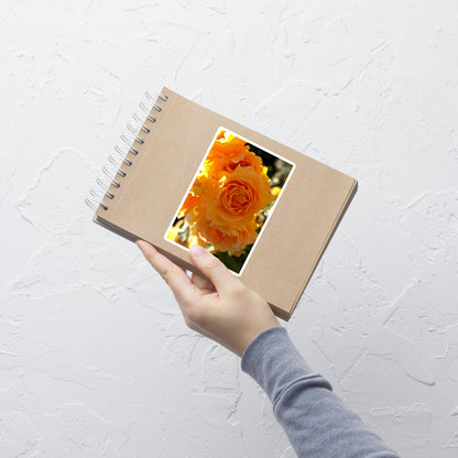 Lifestyle photo of a rectangular vinyl sticker with an image of orange rose blooms, placed on a small notepad.