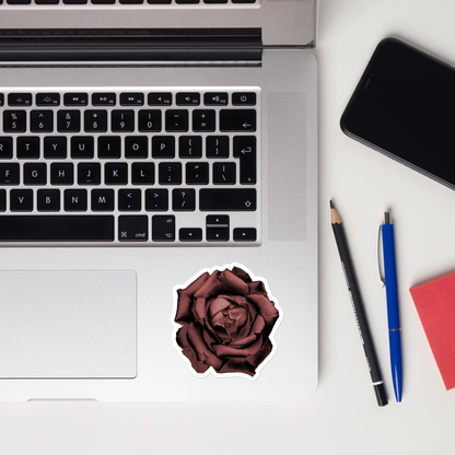 Lifestyle photo of a kiss-cut vinyl sticker with an image of a red charcoal drawing style rose, placed on a laptop to the right of the mouse pad.