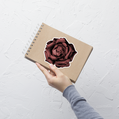 Lifestyle photo of a kiss-cut vinyl sticker with an image of a red charcoal drawing style rose, placed on a small notepad.