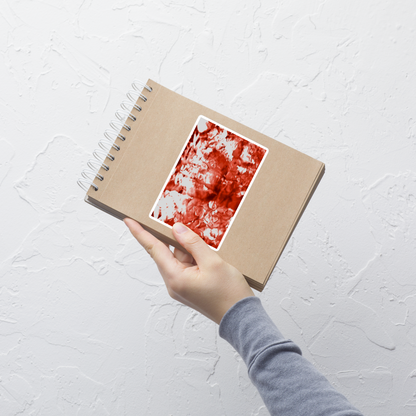 Lifestyle photo of a rectangular vinyl sticker with an image of a vivid red water reflection design, placed on a small notepad.