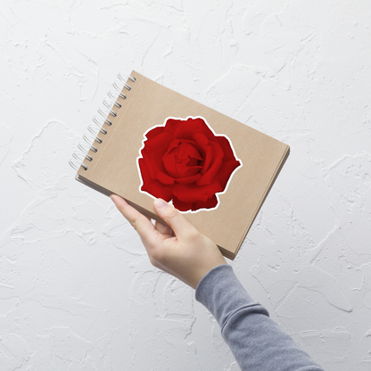 Lifestyle photo of a kiss-cut vinyl sticker with an image of a vivid red rose design, placed on a small notepad.
