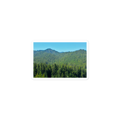 A small rectangular vinyl sticker with an image of mountain landscape with redwood trees and blue sky.