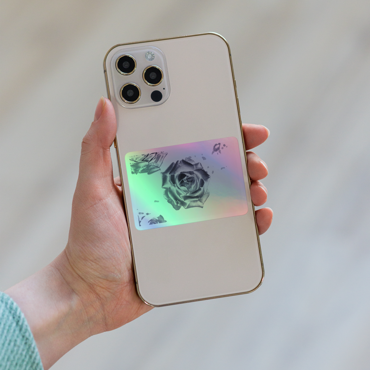 Lifestyle photo of a rectangular holographic sticker with an image of a silver reflective rose design, placed on the back of a phone.