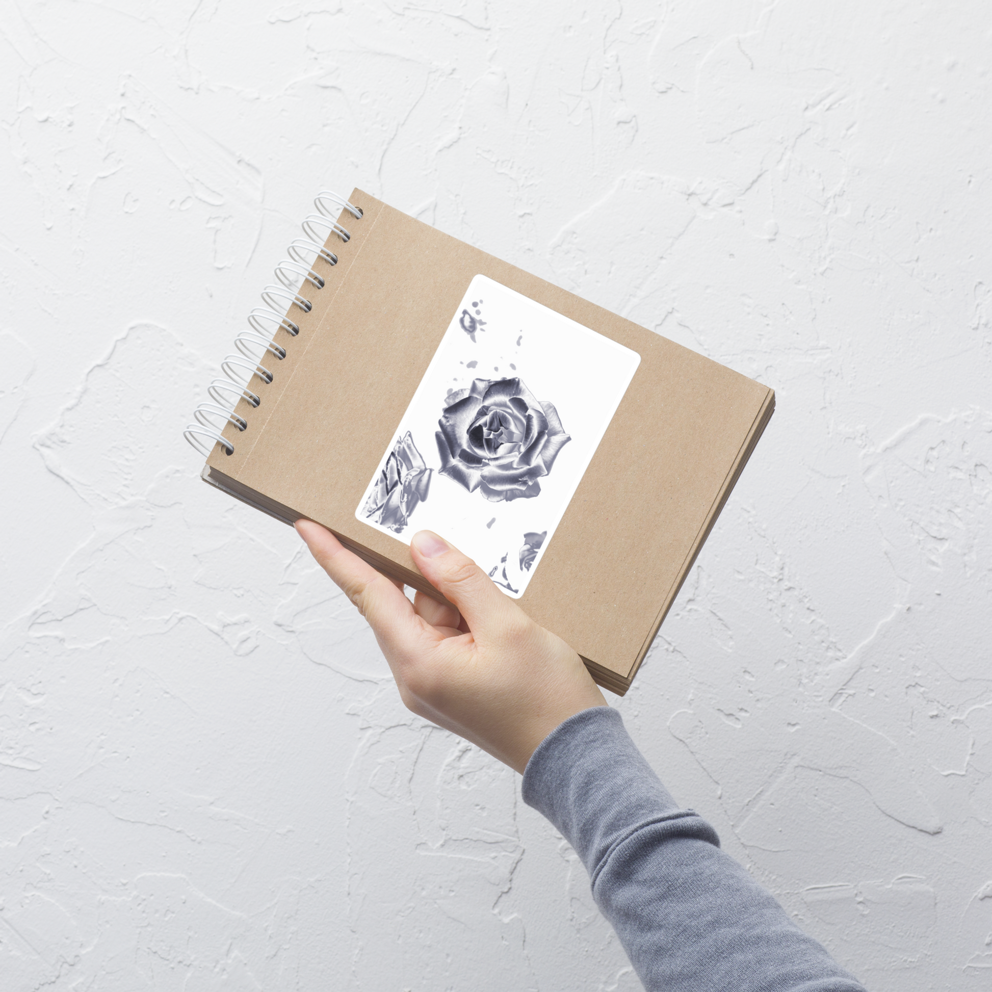 Lifestyle photo of a rectangular vinyl sticker with an image of a reflective silver rose design, placed on a small notepad.
