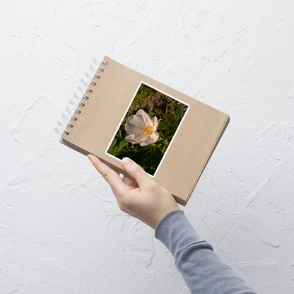Lifestyle photo of a rectangular vinyl sticker with an image of white rose bloom with yellow stamen, placed on a small notepad.