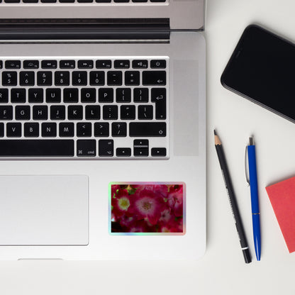Lifestyle photo of a rectangular holographic sticker with an image of pink rose blooms with white centers, placed on a laptop to the right of the mouse pad.