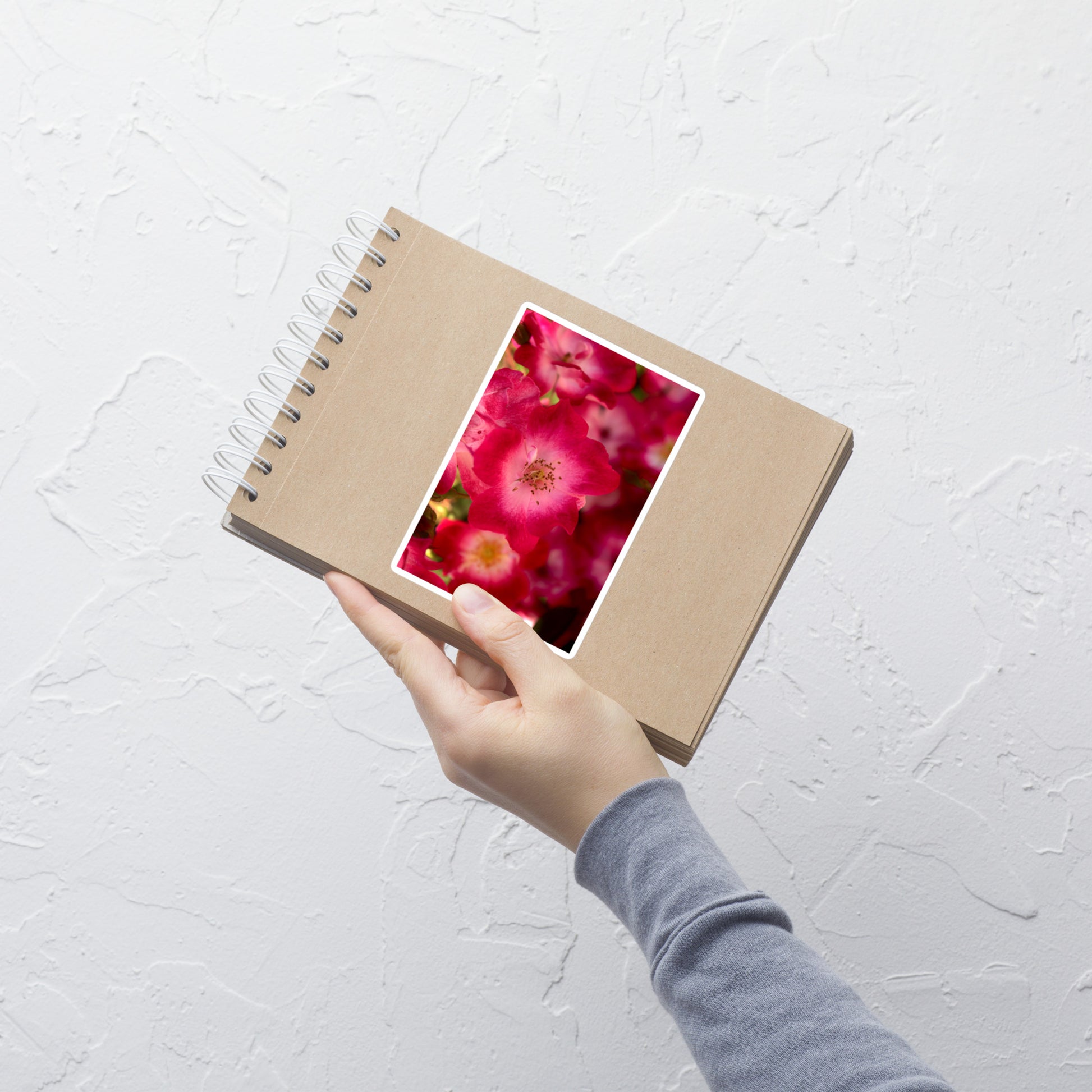 Lifestyle photo of a rectangular vinyl sticker with an image of dark pink flowers with white centers, placed on a small notepad.