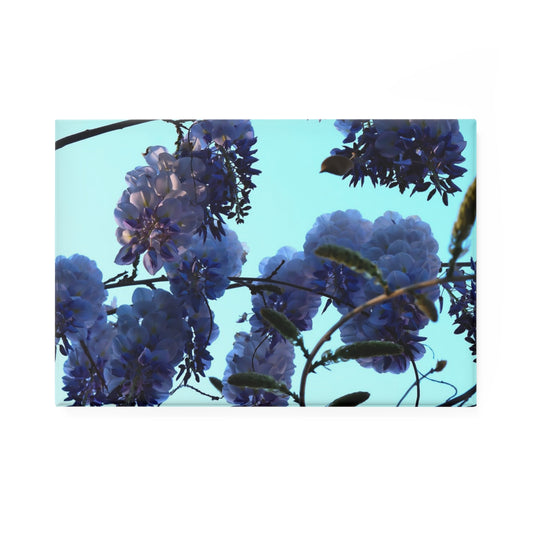 A rectangular button magnet featuring an image of purple wisteria blossoms against a clear blue sky.