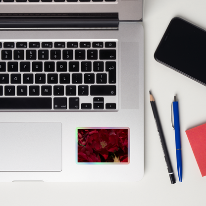 Lifestyle photo of a rectangular holographic sticker with a close-up image of dark red roses, placed on a laptop to the right of the mouse pad.
