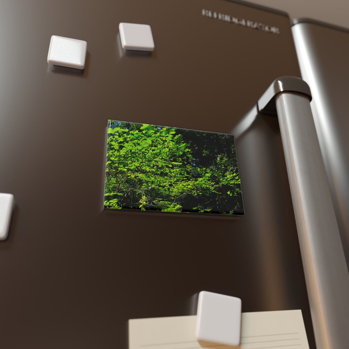 Lifestyle photo of a rectangular button magnet with an image of sunlight streaming through green tree leaves, placed on a fridge.