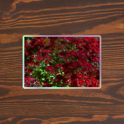 Lifestyle photo of a rectangular holographic sticker with an image of many small, bright red flowers, placed on a brown wooden table surface.