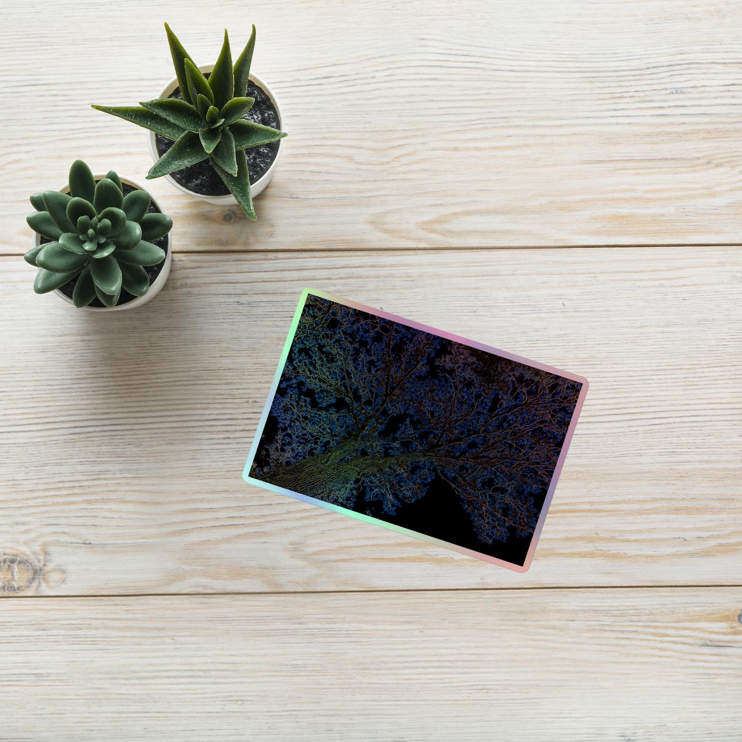 Lifestyle photo of a rectangular holographic sticker with an image of a yellow and blue neon tree lightning design, placed on a table with two small succulents.